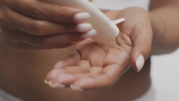 Koncepcja pielęgnacji ciała. Nierozpoznawalna Afroamerykanka wyciskająca krem nawilżający na dłoń z rurki - Materiał filmowy, wideo