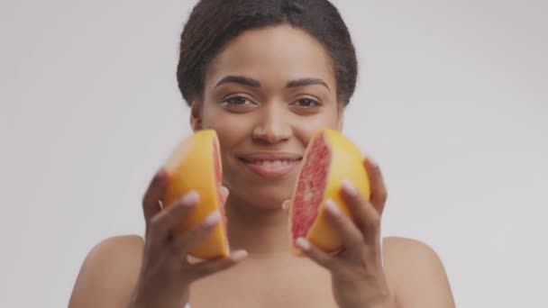 Young african american woman dividing grapefruit into halves and smiling to camera, white studio background, slow motion - Felvétel, videó