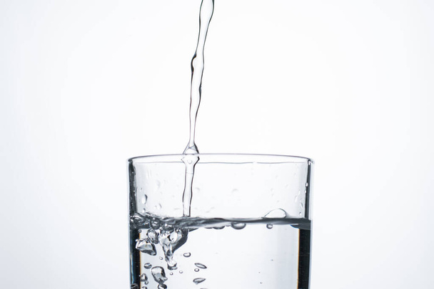 Wasserstrahl oder Alkohol ergießt sich in ein Glas mit Spritzern und Blasen, Kopierraum. - Foto, Bild