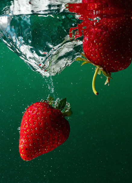 спелые клубники падают в воду, поднимая брызги и пузыри воздуха - Фото, изображение