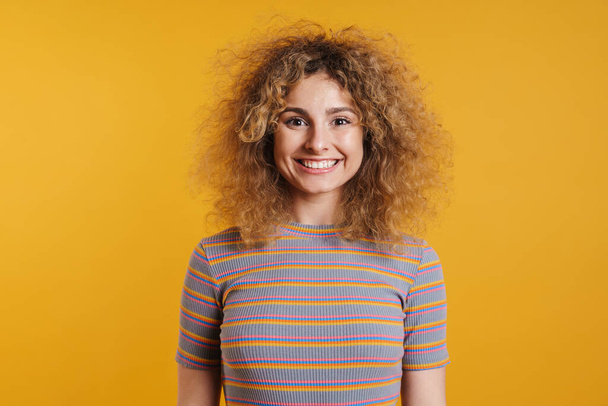 Feliz sorrindo jovem loira mulher com cabelo esbugalhado em roupas casuais em pé sobre fundo de parede amarela, olhando para a câmera - Foto, Imagem
