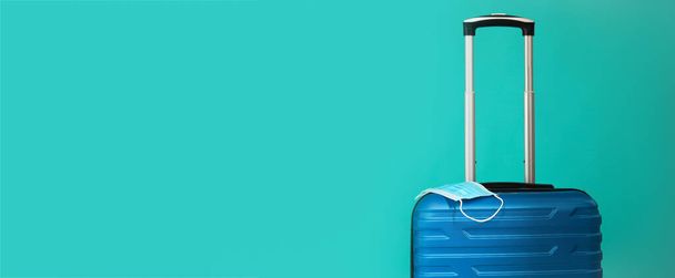 Travel during the time of COVID-19. Blue suitcase with medical mask on the blue background. Free space for text copy space. Vacation, holidays in corona times. - 写真・画像