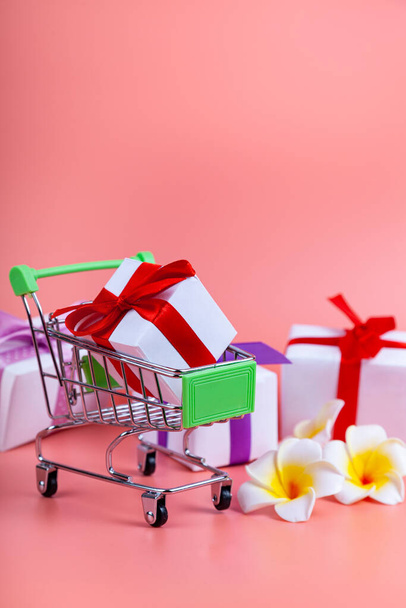Shopping cart and gifts on a pink background. Concept: buying gifts. - Фото, изображение