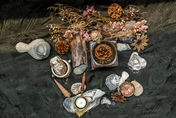 Kosmetické složení s hořící svíčkovou olejovou lampou a okvětními lístky suchých květin a borovými šiškami, kotoučem z přírodního borového dřeva, kameny a mušlemi, himálajskou solí na tmavém pozadí. Aromaterapeutický koncept. - Fotografie, Obrázek