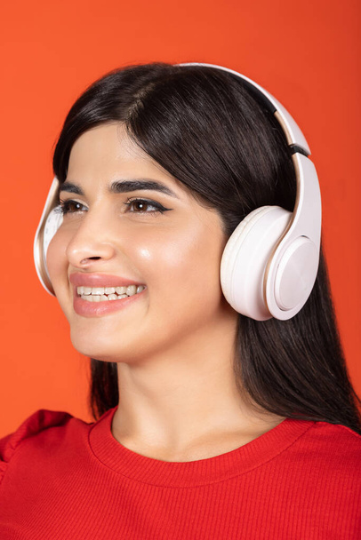 Detailní oříznutý portrét mladé krásné dívky ve sluchátkách izolovaných přes oranžové pozadí. - Fotografie, Obrázek
