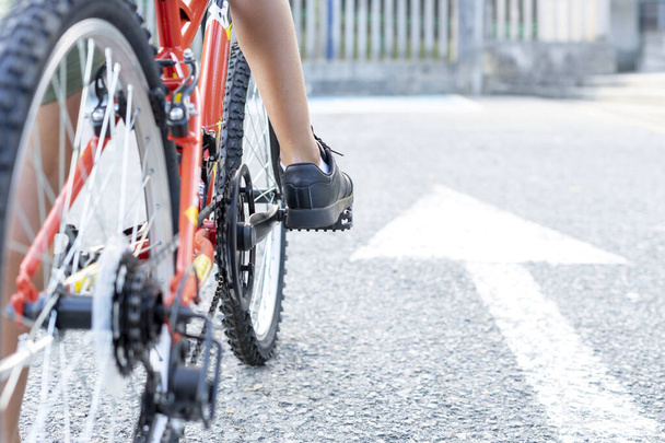 Primo piano di un bambino gambe montate sulla sua bicicletta pronto a iniziare a cavalcare accanto a un cartello freccia bianca dipinta a terra che indica andare avanti. Concetto Continua ad andare avanti - Foto, immagini