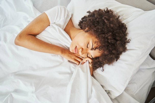 Hermosa mujer serena con cabello rizado dormitando en la almohada - Foto, Imagen