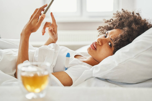 Niskowystarczalna piękna kobieta leżąca w łóżku podczas pomiaru temperatury - Zdjęcie, obraz