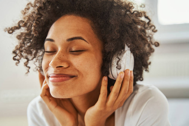 Smiling pleased dark-haired female wearing wireless headphones - Photo, Image