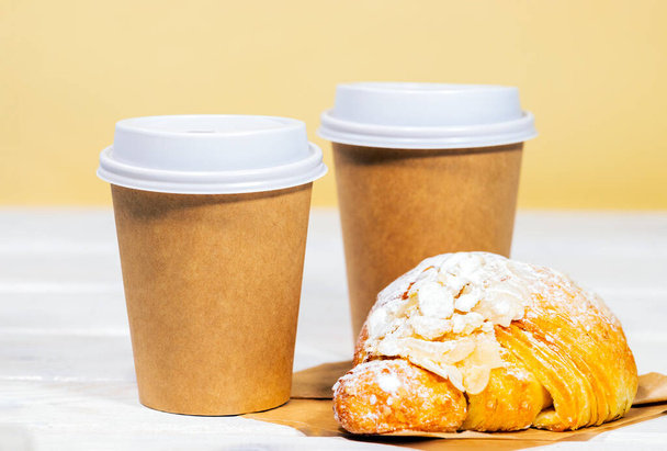 Káva jít v papírové eko šálek s mandlovým croissant na dřevěném a světle oranžovém pozadí, Rychlé občerstvení, Copyspace, Kofein Nápoj odnést - Fotografie, Obrázek