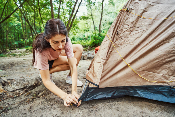 Active young woman fixing tent in wood - Foto, imagen