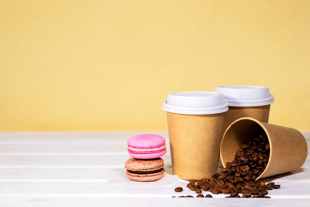 Koffie te gaan in papieren eco cup met chocolade franse macaroon op houten en licht oranje achtergrond, Fast food, Copyspace, Cafeïne Drink meeneem - Foto, afbeelding
