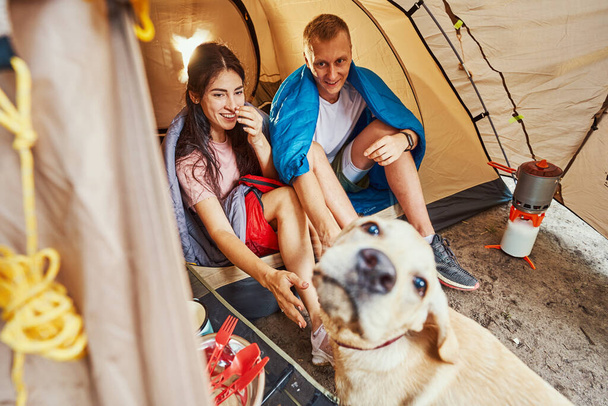 Happy couple having fun with dog in camp - Photo, Image
