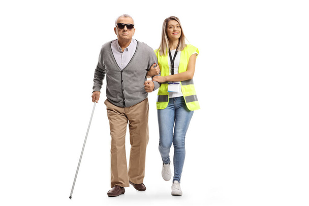 Ολόκληρο το πορτραίτο μιας εργαζόμενης της κοινότητας που βοηθά έναν ηλικιωμένο τυφλό άνδρα απομονωμένο σε λευκό φόντο - Φωτογραφία, εικόνα