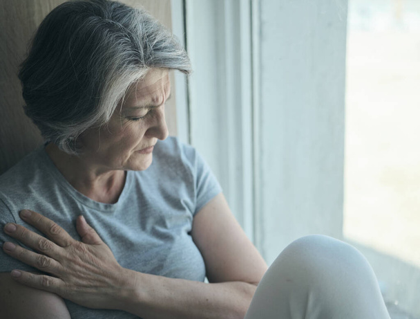 Starszy starszy starszy chory niepełnosprawny, smutna kobieta w bólu i cierpieniu siedzi przy oknie w szpitalu. - Zdjęcie, obraz