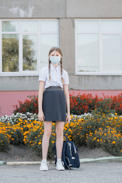 Child with face mask going back to school after covid-19 quarantine and lockdown. Back to school university student girl wearing covid mask walking on campus with backpack, books and laptop - 写真・画像