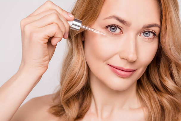 Portrait of attractive woman applying serum under eye freshness uplift effect isolated over grey pastel color background - Φωτογραφία, εικόνα