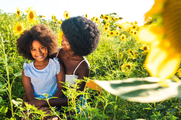 Bela mãe afro-americana e filha pálido e se divertindo em um campo de girassóis - Foto, Imagem
