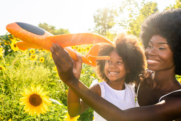 Beautiful afro-american mom and daughter palying and having fun in a sunflowers field - Fotografie, Obrázek