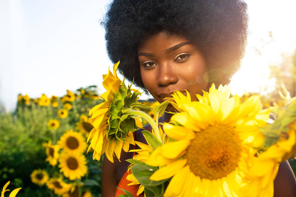 Beautiful afro-american woman with curly afro style hair in a sunflowers field - Valokuva, kuva