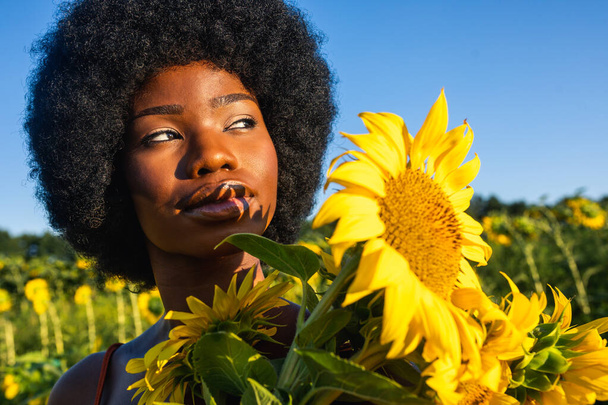 Beautiful afro-american woman with curly afro style hair in a sunflowers field - Fotografie, Obrázek