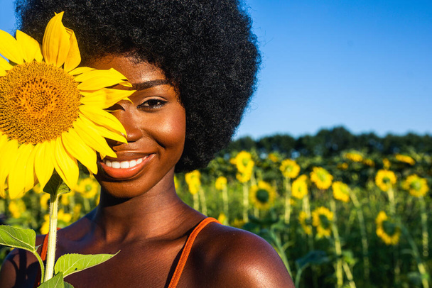 Belle femme afro-américaine avec des cheveux frisés de style afro dans un champ de tournesols - Photo, image