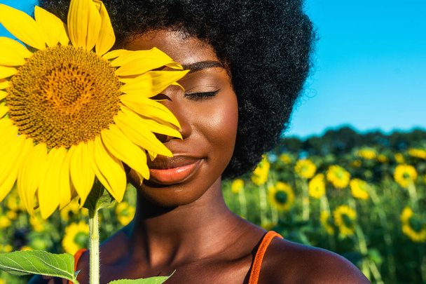 Beautiful afro-american woman with curly afro style hair in a sunflowers field - Fotoğraf, Görsel