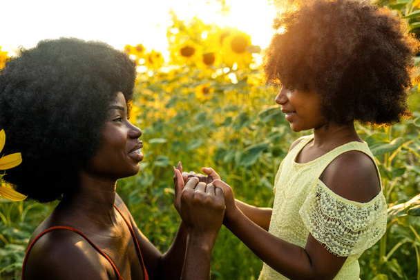 Beautiful afro-american mom and daughter palying and having fun in a sunflowers field - Foto, Imagen