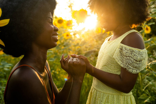 Beautiful afro-american mom and daughter palying and having fun in a sunflowers field - Foto, afbeelding