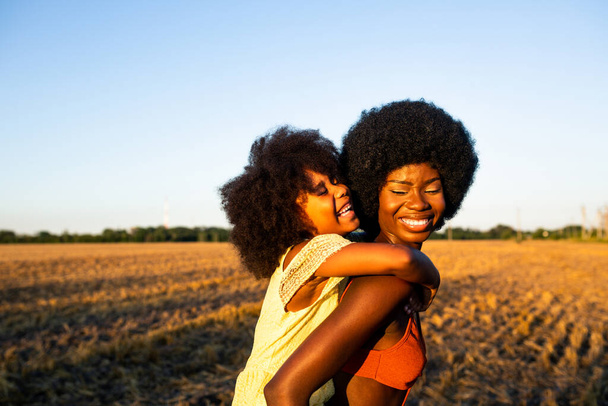 Beautiful afro-american mom and daughter palying and having fun in a sunflowers field - Photo, Image