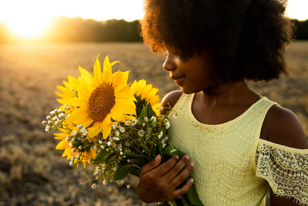 Pretty afro american girl in a sunflowers field having fun - Фото, зображення