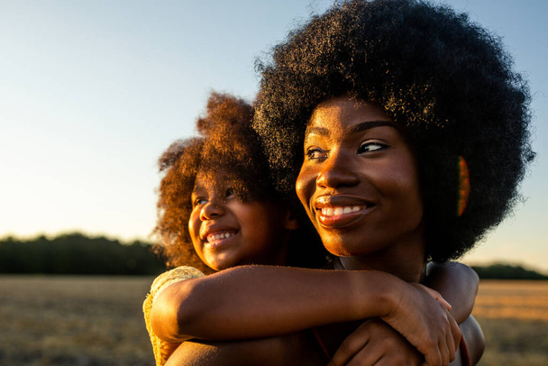 Beautiful afro-american mom and daughter palying and having fun in a sunflowers field - Foto, immagini