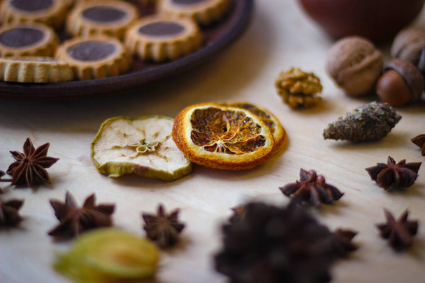 Foto de temporada de otoño. Rodajas secas de naranja, manzana, bellotas, physalis, y en el fondo hay un plato de galletas - Foto, imagen