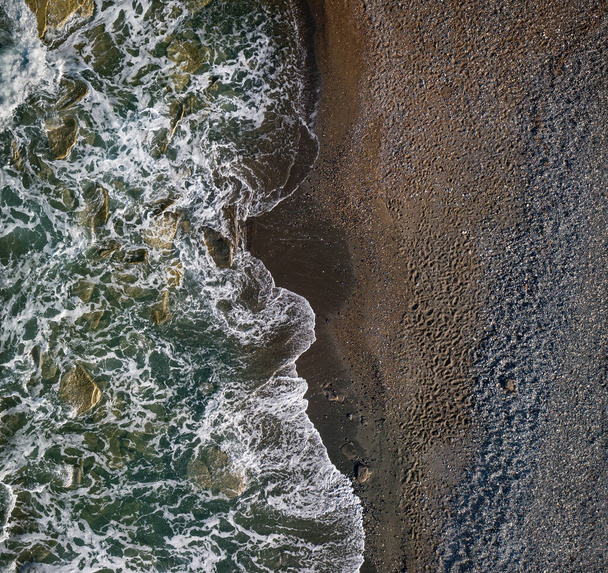 Zelené vlny s bílou mořskou pěnou přes tmavý písečný břeh čokoládové barvy, horní pohled textury - Fotografie, Obrázek