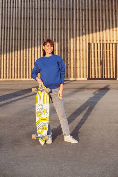 Woman with a skateboard wears blue sweatshirt. - Foto, Imagen