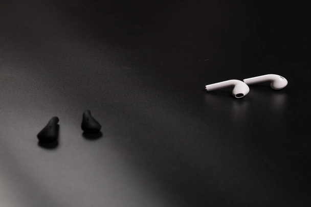 Two pairs of wireless earphone white and black colors, on black background. - Fotografie, Obrázek