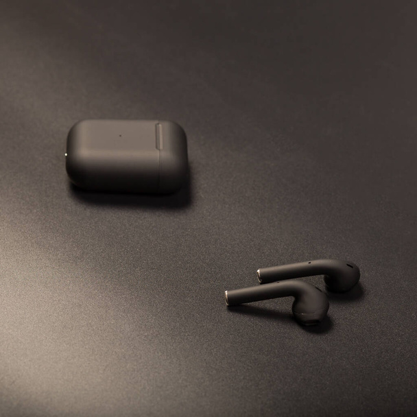 Black wireless earbids with charging case, close up on black background. - Fotografie, Obrázek