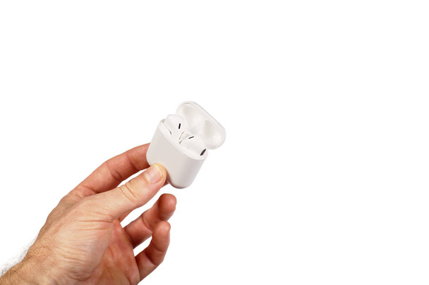 Male hand holding white wireless earphones in charging case, isoalted on a white. - Fotoğraf, Görsel