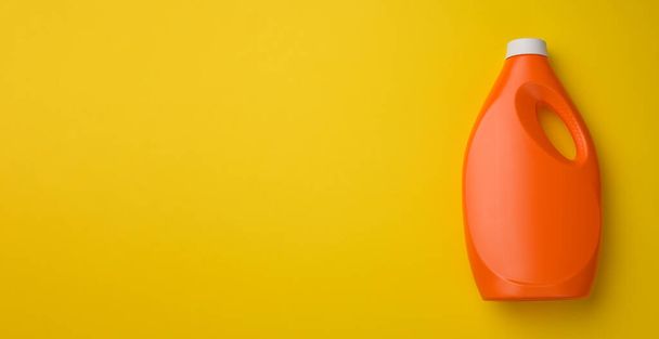оранжевый пластиковый флакон для жидкого стирального порошка на желтом фоне, вид сверху, пространство для копирования - Фото, изображение