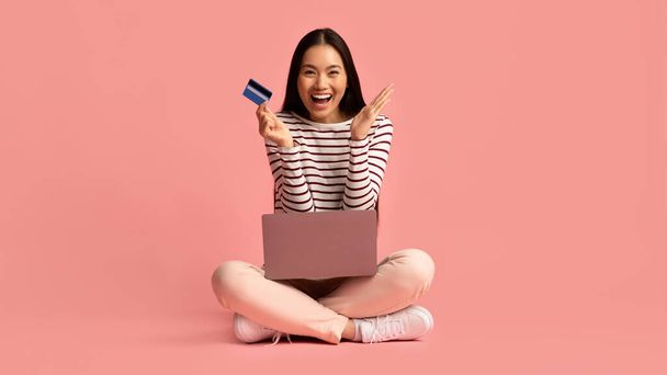 Paiements en ligne. Joyeux jeune asiatique femme assis avec ordinateur portable et carte de crédit - Photo, image
