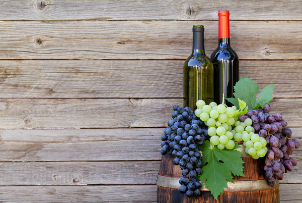 Various colorful grapes and wine bottles on wine barrel on outdoor sunny garden in front of wooden wall with copy space - Valokuva, kuva