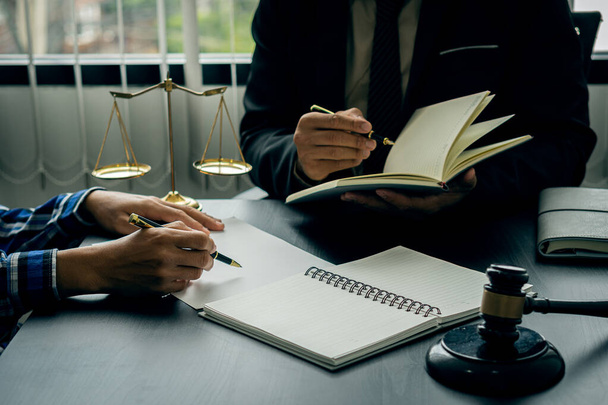 A male lawyer consults a team of legal clients and businessmen who are negotiating contracts. Human hands work with papers at the desk and sign contracts.Keywords: on the table with hammer and scales - Photo, Image
