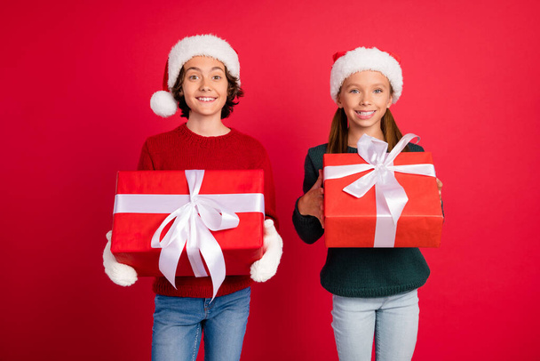 Portrait of two attractive cheerful friends friendship holding giftbox eve December isolated over bright red color background - Фото, изображение