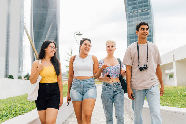 Grupo de jovens multiéticos amigos caminhando ao ar livre conversando e desfrutando de união e boa companhia - Foto, Imagem