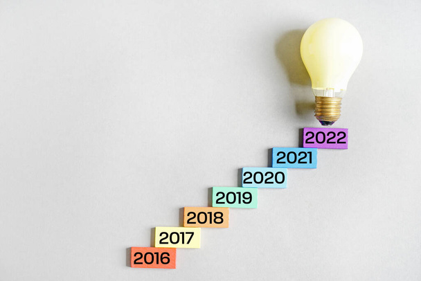 Cijfers voor de jaren 2016-2022 en gloeilamp op grijze achtergrond - Foto, afbeelding