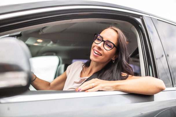 Happy female driver in glasses looks through the open side window of a car she drives.. - Foto, Bild