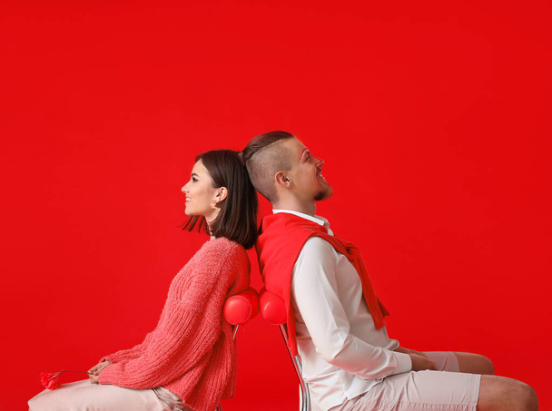 Stílusos fiatal pár ül székek ellen piros háttér - Fotó, kép