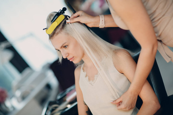 Перукарня, що робить волосся розширенням для молодої жінки з світлим волоссям в салоні краси. Професійне нарощування волосся нитками
. - Фото, зображення