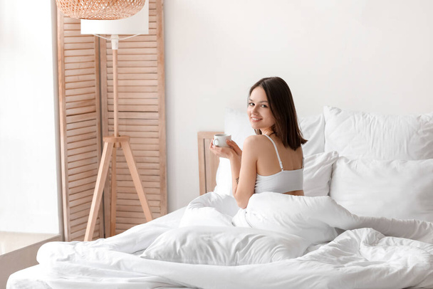 Young woman drinking coffee in bedroom - Fotó, kép