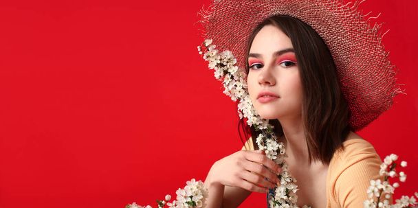 Beautiful young woman with blooming spring branches on red background - Photo, Image